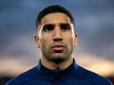 Portrait de face du footballeur Achraf Hakimi portant un haut bleu foncé sur fond flou
