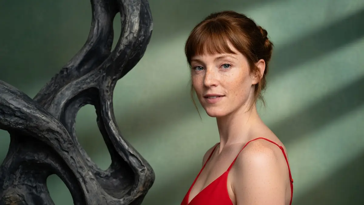Portrait de l'actrice Alexandra Cismondi posant en robe rouge devant une sculpture organique sur fond vert