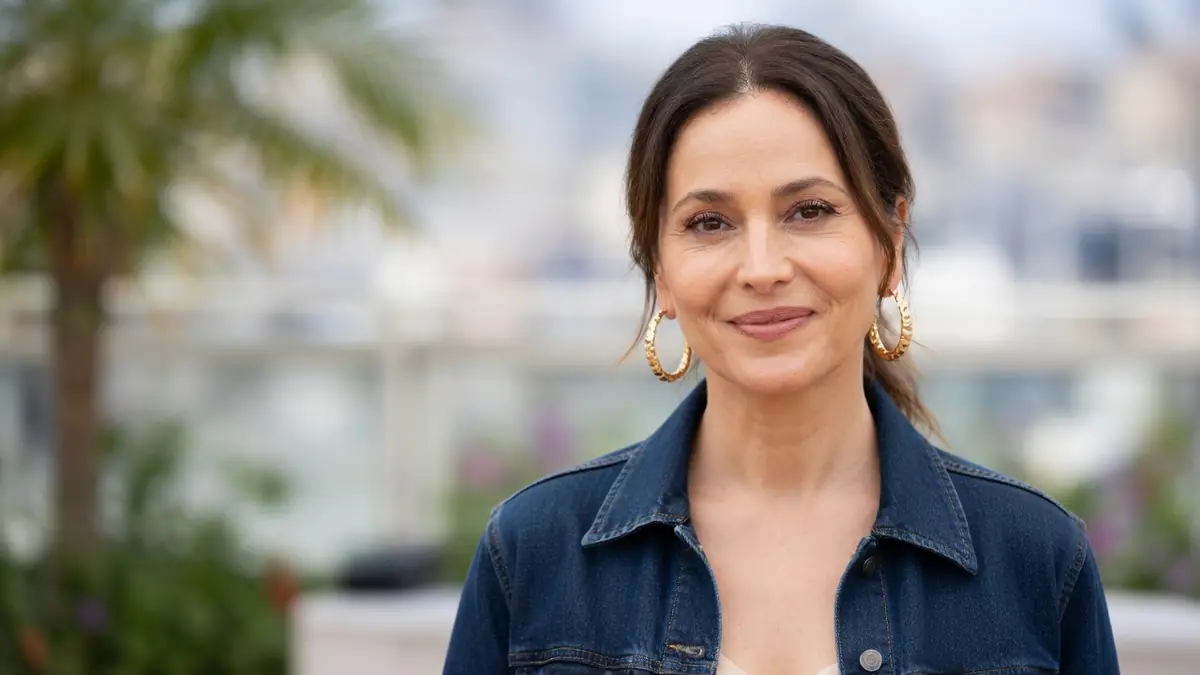 Anne Charrier arbore un léger sourire vêtue d'une veste en jean et de boucles d'oreilles dorées.