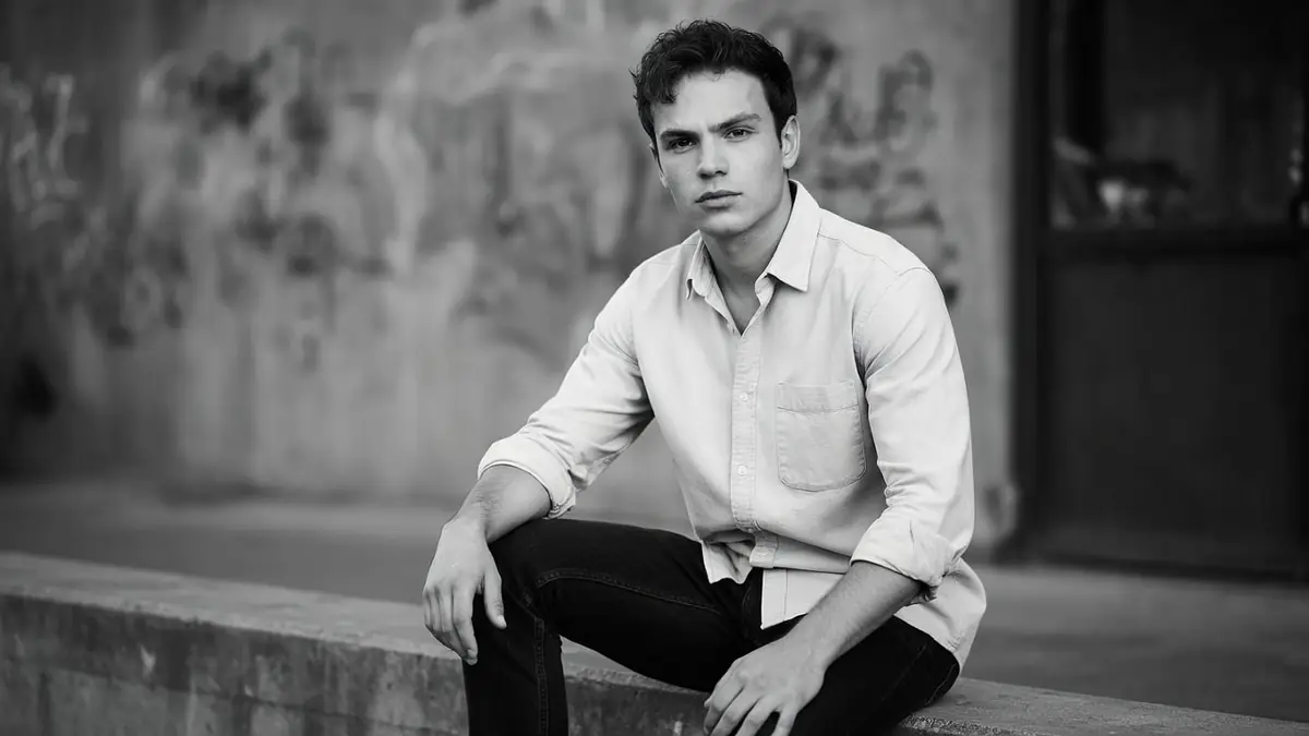 Portrait en noir et blanc de l'artiste Antoine Simony assis sur un muret dans un environnement urbain