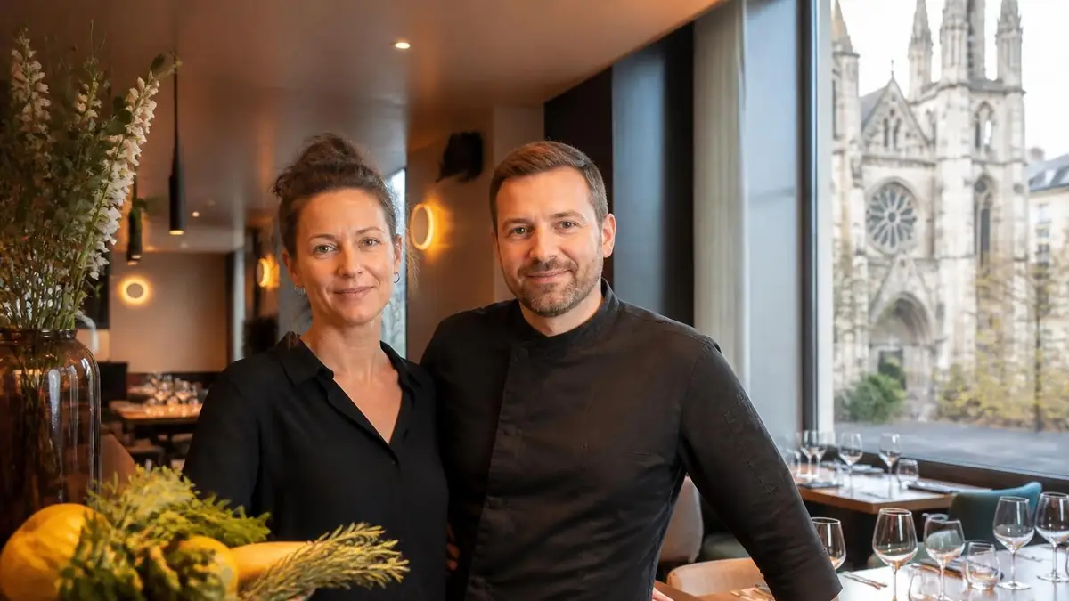 Un couple de restaurateurs souriants dans leur établissement situé au coins de la rue avec une église en arrière-plan