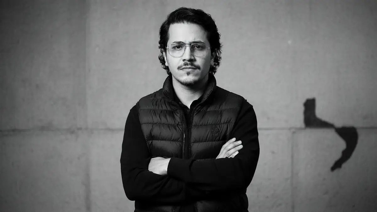 Portrait en noir et blanc de l'acteur Brahim Bouhlel posant les bras croisés devant un mur gris