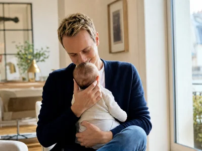 Cyril Féraud en couple serre son bébé contre lui dans un salon lumineux.