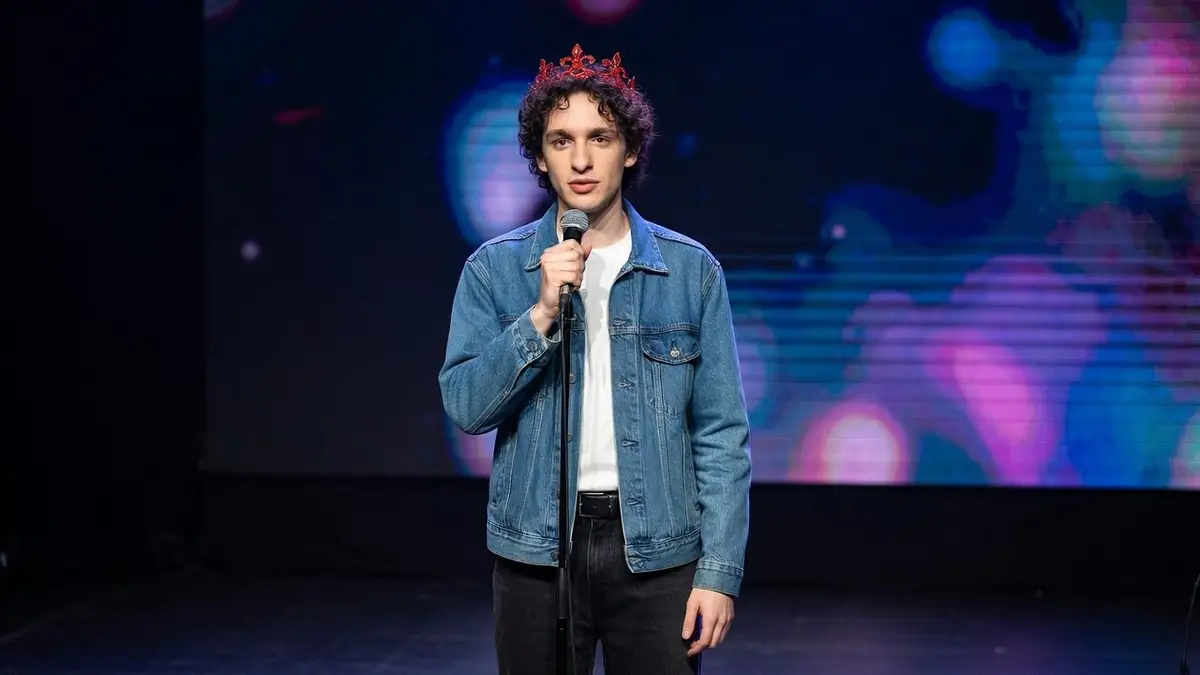 Léo Rispal se tient sur scène avec un micro à la main et une couronne sur la tête