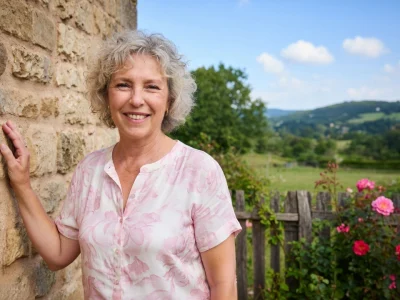 Olivia Adriaco se tient souriante contre un mur en pierre dans un jardin du Pays basque