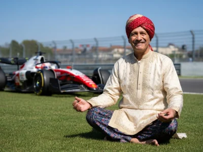 Eric Bhat médite en tailleur sur l'herbe près d'une voiture de Formule 1