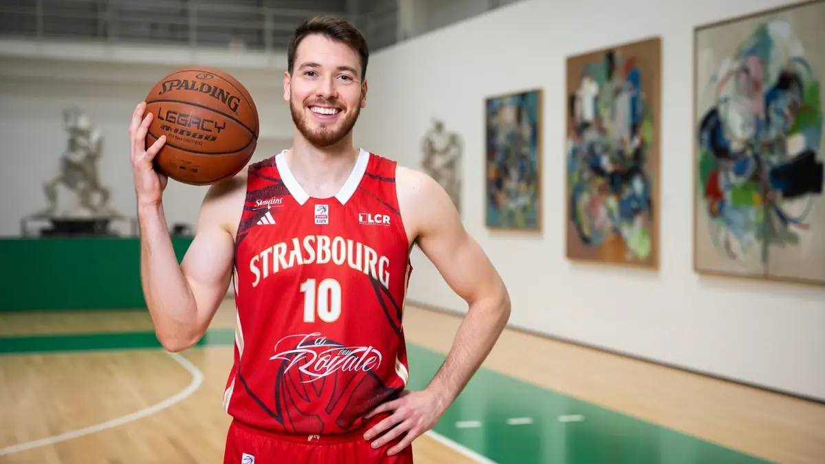 Hugo Invernizzi pose avec un ballon de basket dans une salle de sport