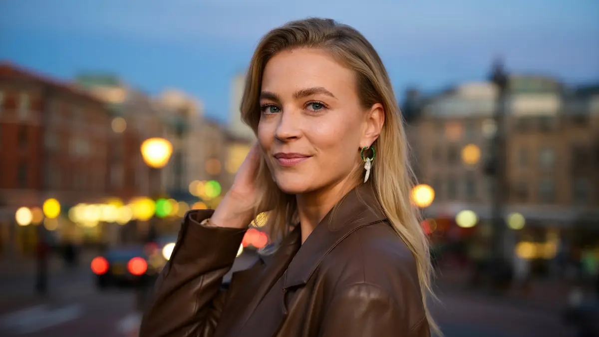 Jeanne Goursaud pose en veste marron dans une rue urbaine illuminée le soir.