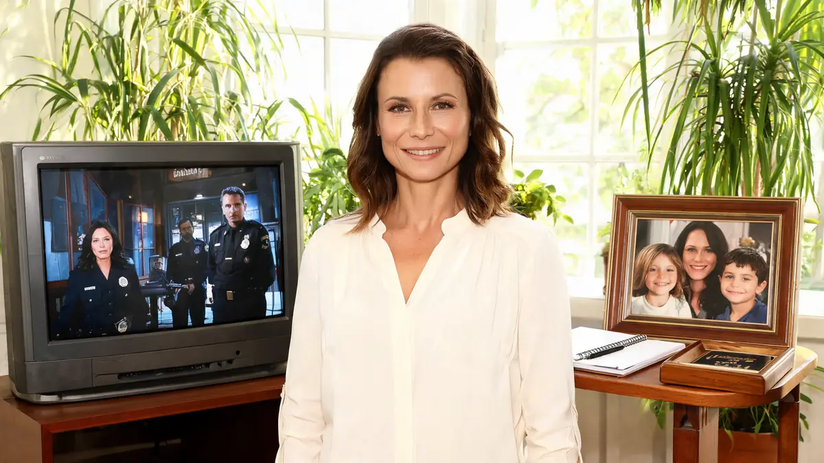 Jennifer Lauret se tient dans une pièce lumineuse entre une télévision et une photo de famille encadrée