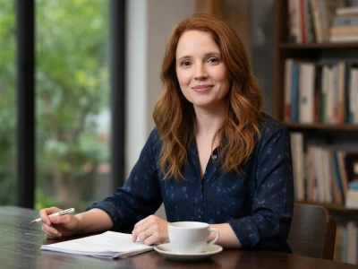 Juliet Lemonnier souriante assise à une table avec un carnet et une tasse de café dans un bureau chaleureux