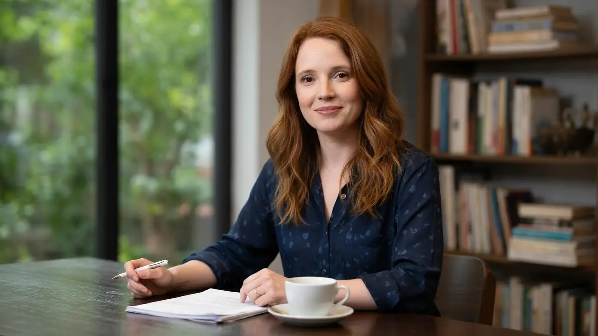 Juliet Lemonnier souriante assise à une table avec un carnet et une tasse de café dans un bureau chaleureux