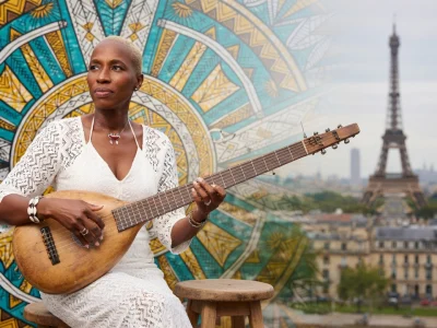Kadi Diarra joue d'un instrument traditionnel devant un motif coloré et la tour Eiffel en arrière-plan