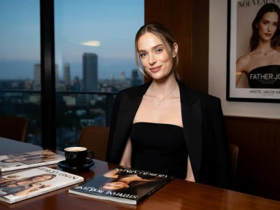 Kristel van de Kamp assise à une table avec des magazines devant une vue sur la ville