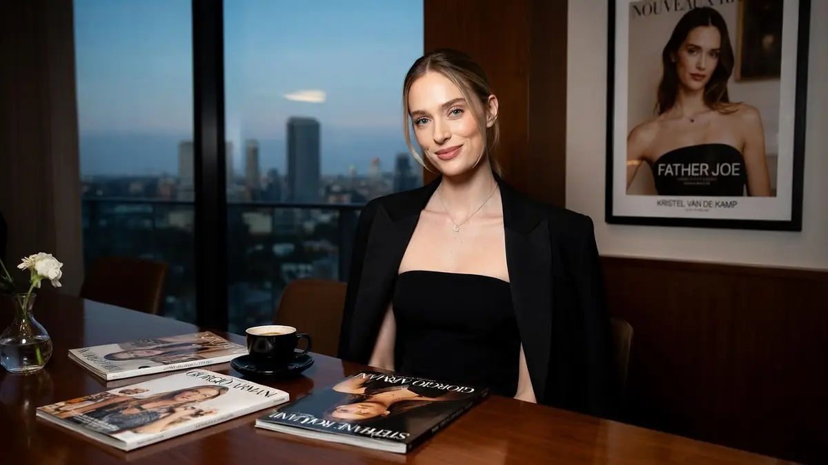 Kristel van de Kamp assise à une table avec des magazines devant une vue sur la ville