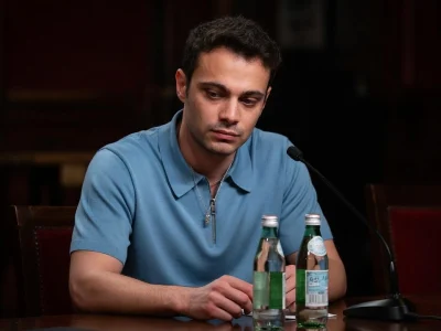 L'acteur Sofiane Bennacer assis à une table lors d'une conférence de presse devant un micro et des bouteilles d'eau