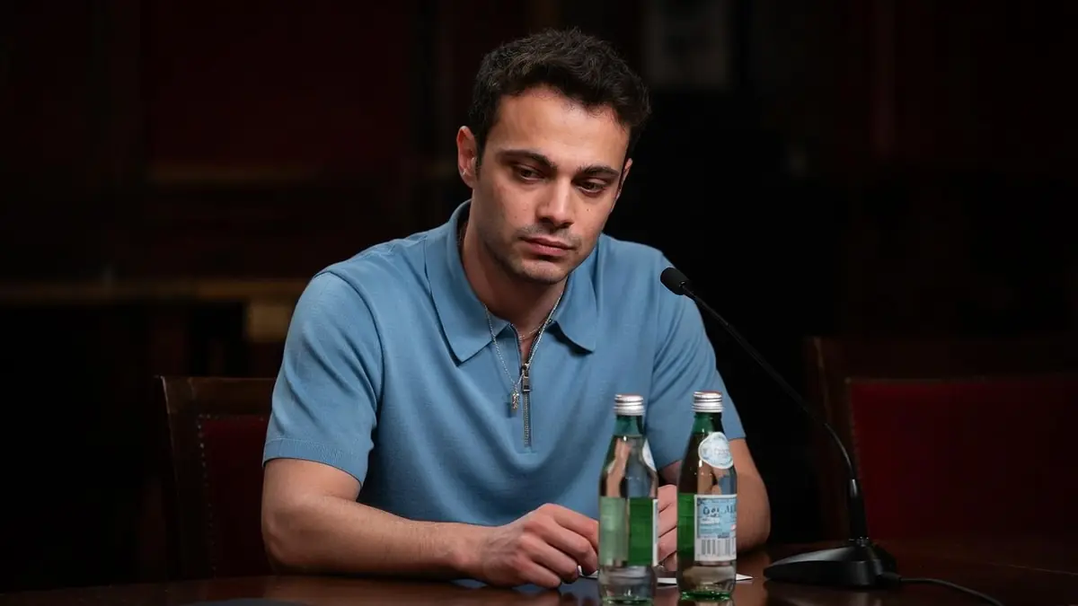 L'acteur Sofiane Bennacer assis à une table lors d'une conférence de presse devant un micro et des bouteilles d'eau