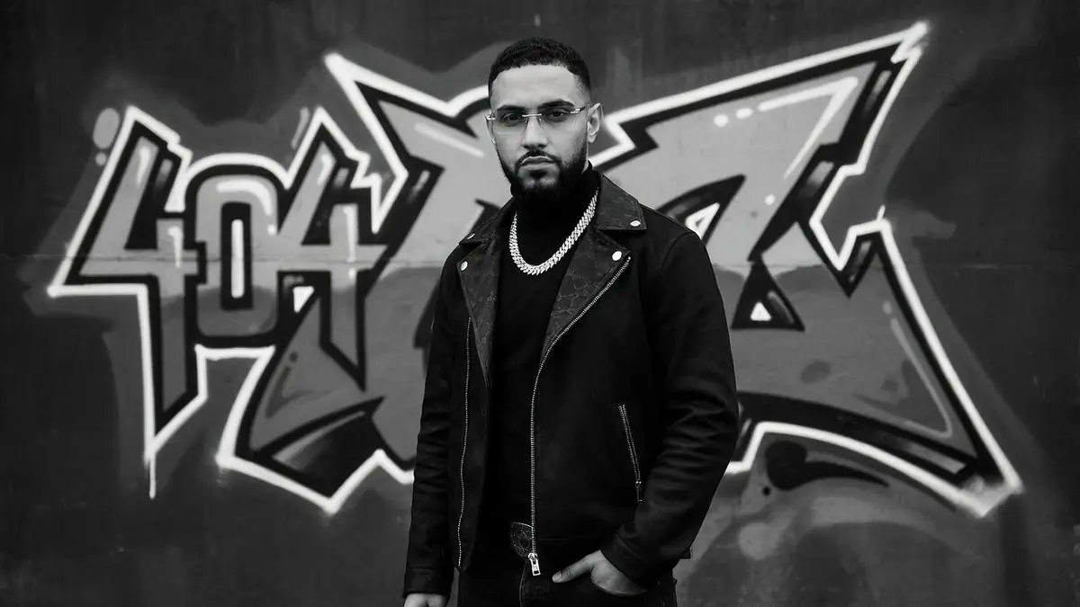 404Billy se tient la main dans la poche en blouson de cuir et collier