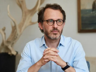 Emmanuel Marre est photographié les mains croisées, portant une chemise bleue et des lunettes