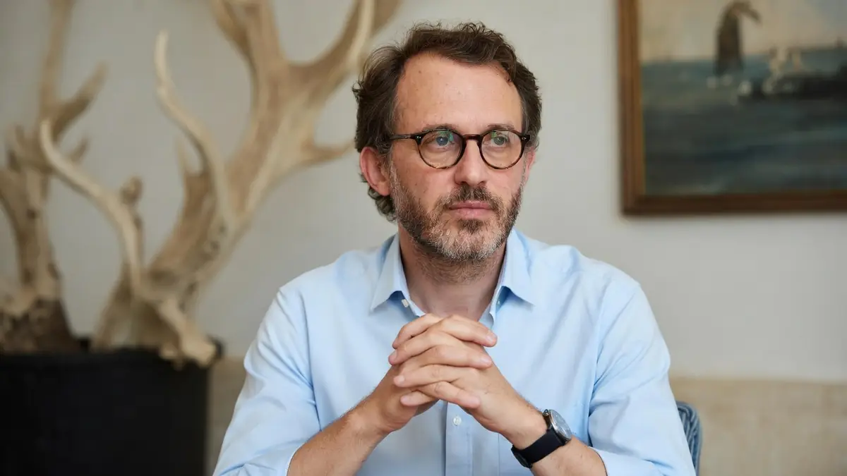 Emmanuel Marre est photographié les mains croisées, portant une chemise bleue et des lunettes
