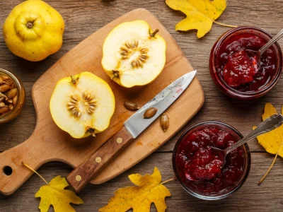 Des coings coupés sur une planche près de bocaux de confit de coing et de feuilles d'automne