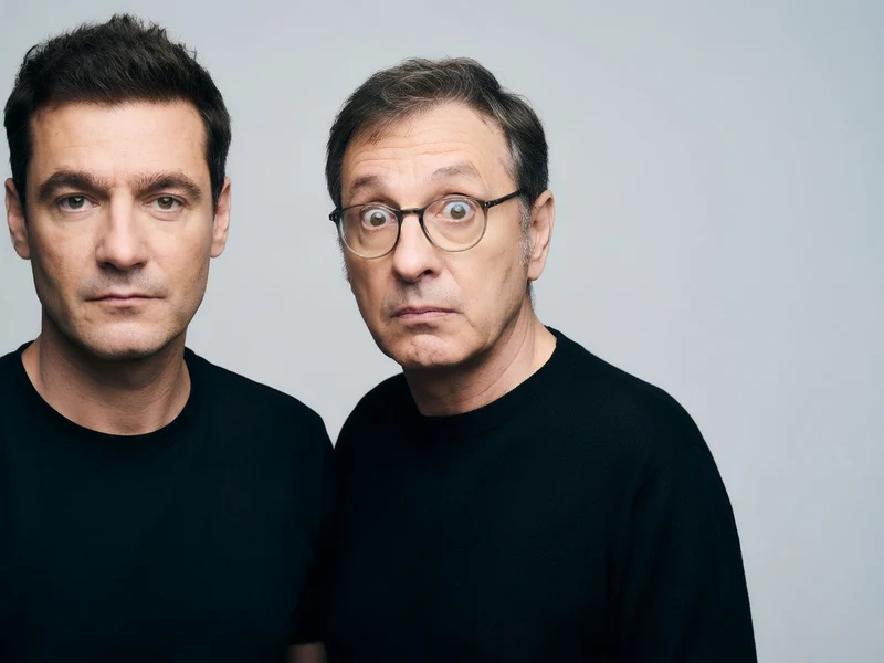 Manu Joucla pose avec un autre homme, l'un sérieux et l'autre faisant une grimace