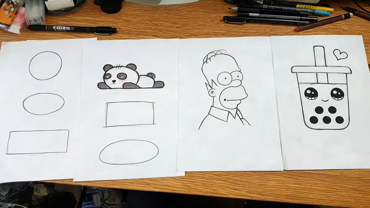 Plusieurs feuilles de papier posées sur un bureau présentent des exemples de dessin facile comme un panda ou un personnage