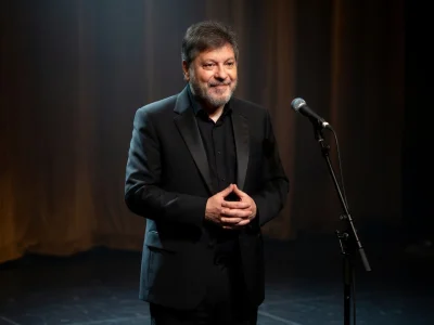 Régis Laspalès se tient les mains croisées sur scène près d'un micro
