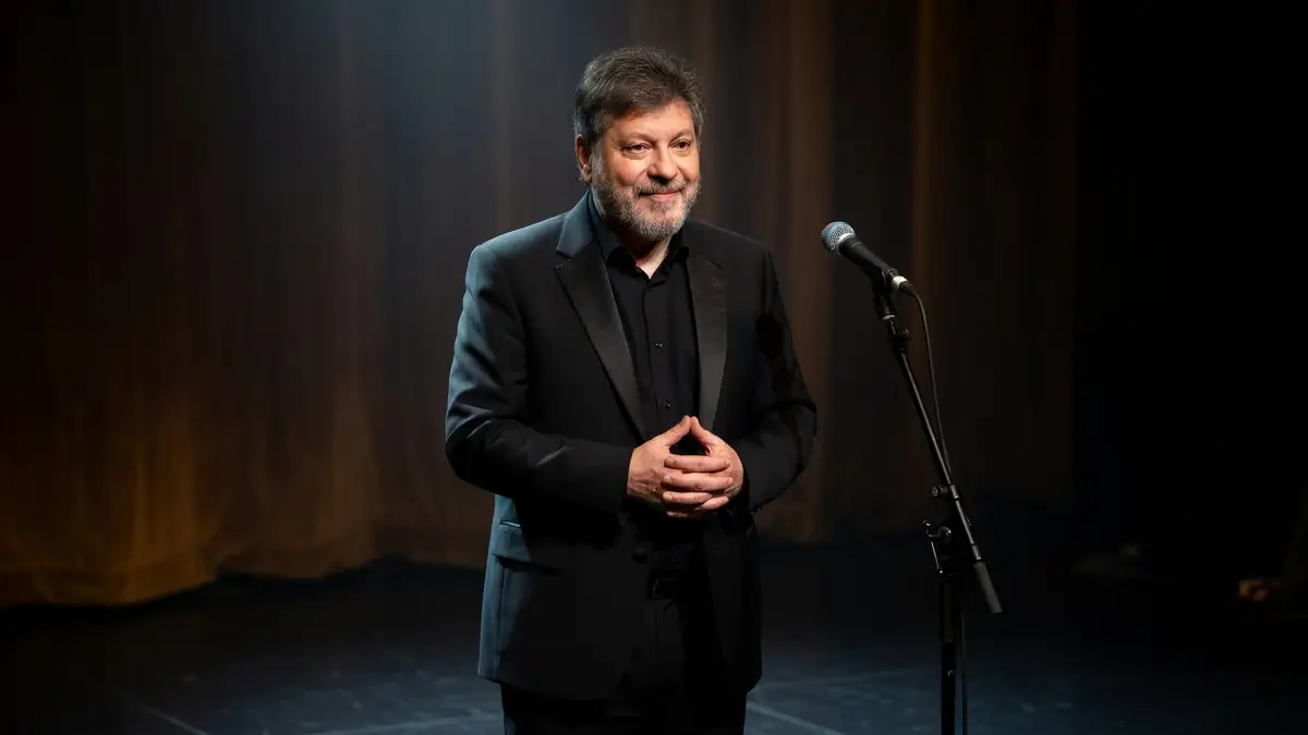 Régis Laspalès se tient les mains croisées sur scène près d'un micro