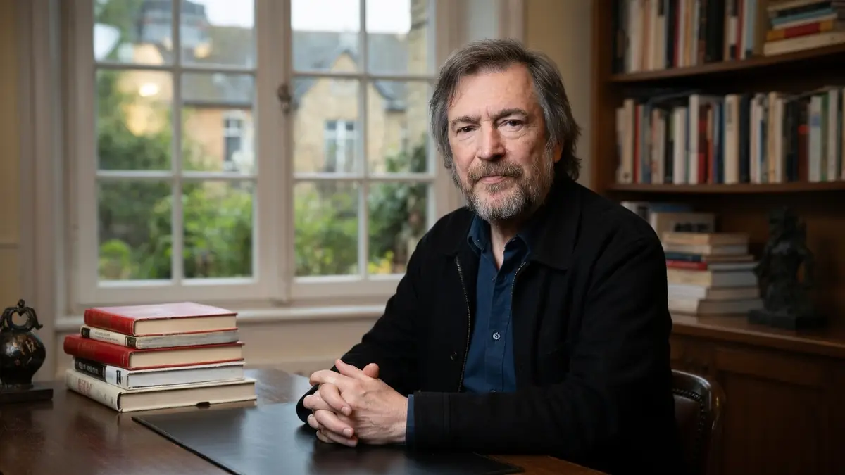 François Chattot est assis à une table dans une bibliothèque remplie de livres