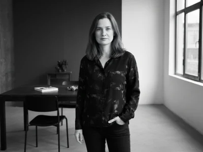 Chloé Dabert se tient dans une pièce minimaliste devant une table et une grande fenêtre