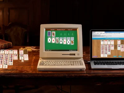 Un ordinateur rétro et un portable montrent le jeu gratuit en ligne Le Solitaire sur une table en bois entourée de cartes