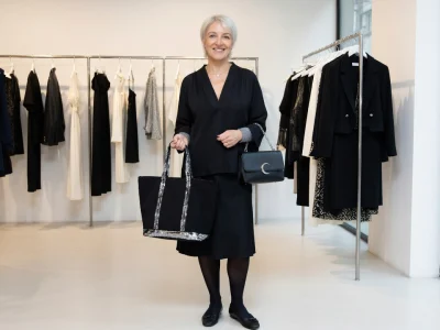 Vanessa Bruno sourit en tenant deux sacs dans un magasin de vêtements