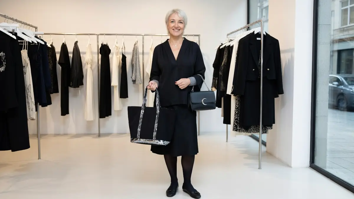 Vanessa Bruno sourit en tenant deux sacs dans un magasin de vêtements