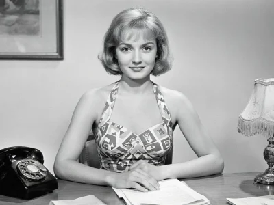 Brigitte Auber est photographiée assise à un bureau avec un téléphone et une lampe