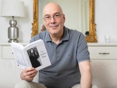 Phil Baron sourit en tenant un livre ouvert sur un canapé