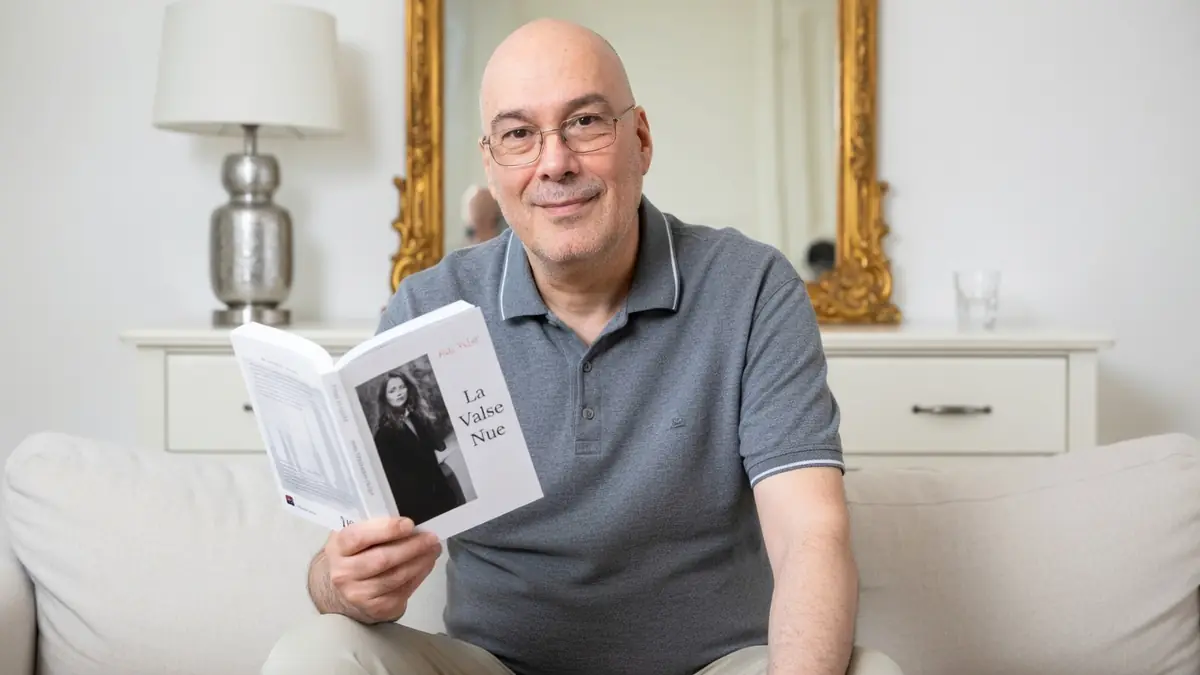 Phil Baron sourit en tenant un livre ouvert sur un canapé