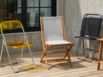 Trois chaises pliantes de différents modèles sont exposées sur une terrasse en bois