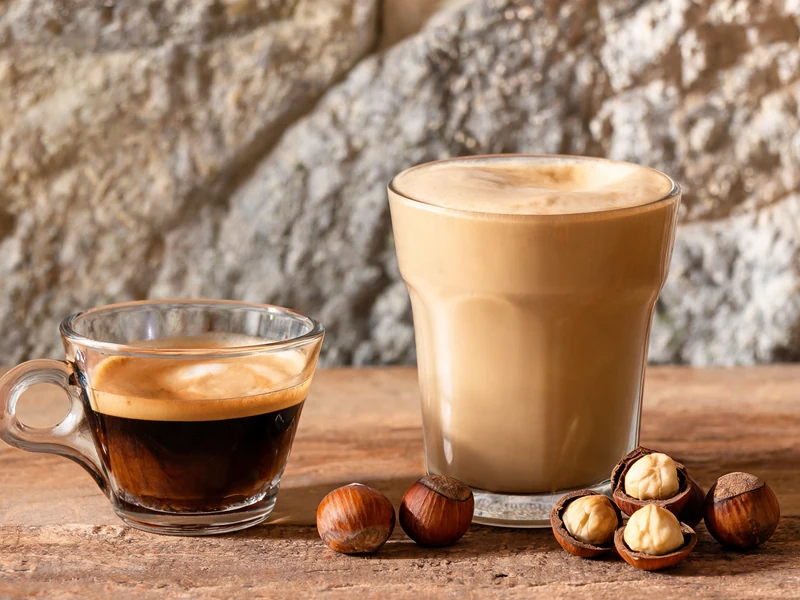 Deux verres de café dont un café à la noisette accompagnés de noisettes sur une table en bois