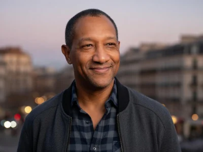 Édouard Montoute sourit dans une rue parisienne au crépuscule