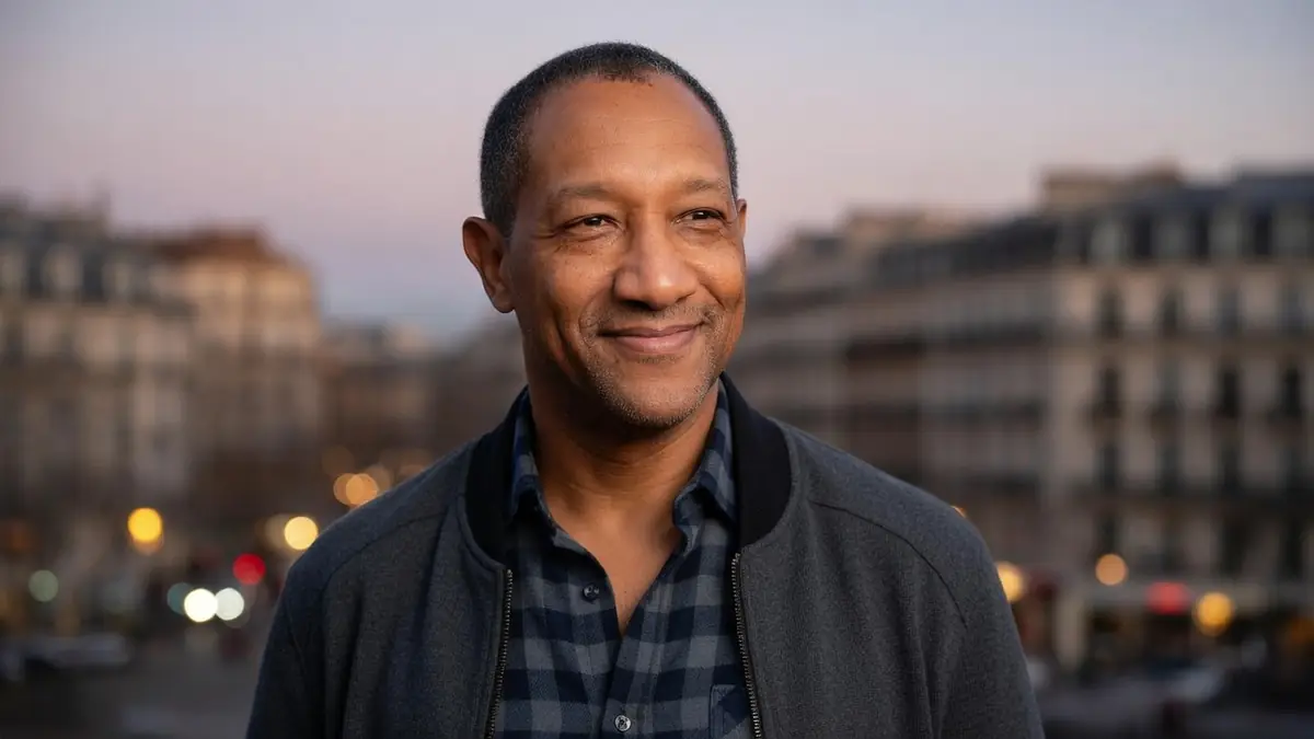 Édouard Montoute sourit dans une rue parisienne au crépuscule