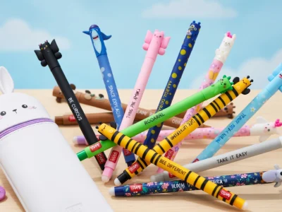 Des Legami stylo colorés avec des têtes d'animaux sont étalés devant une trousse lapin blanche