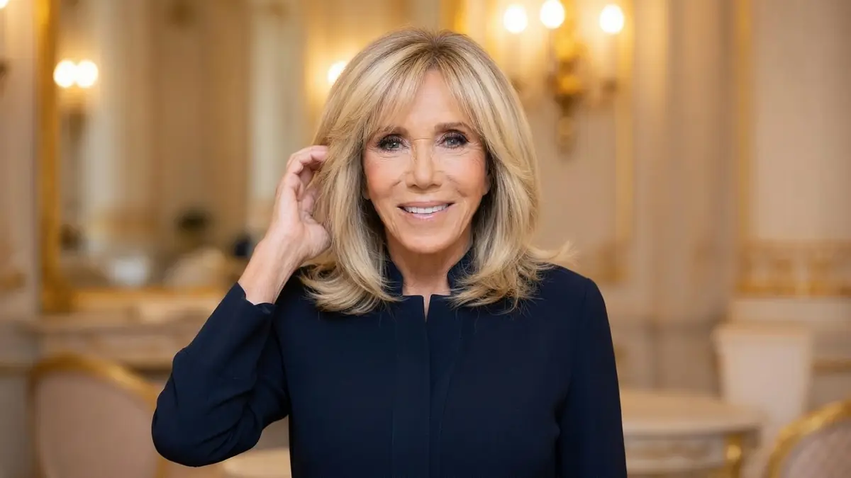 Brigitte Macron perruque touche ses cheveux en souriant dans un décor élégant