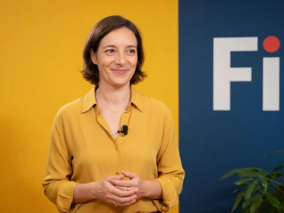 Céline Asselot se tient les mains jointes devant un fond jaune et bleu.