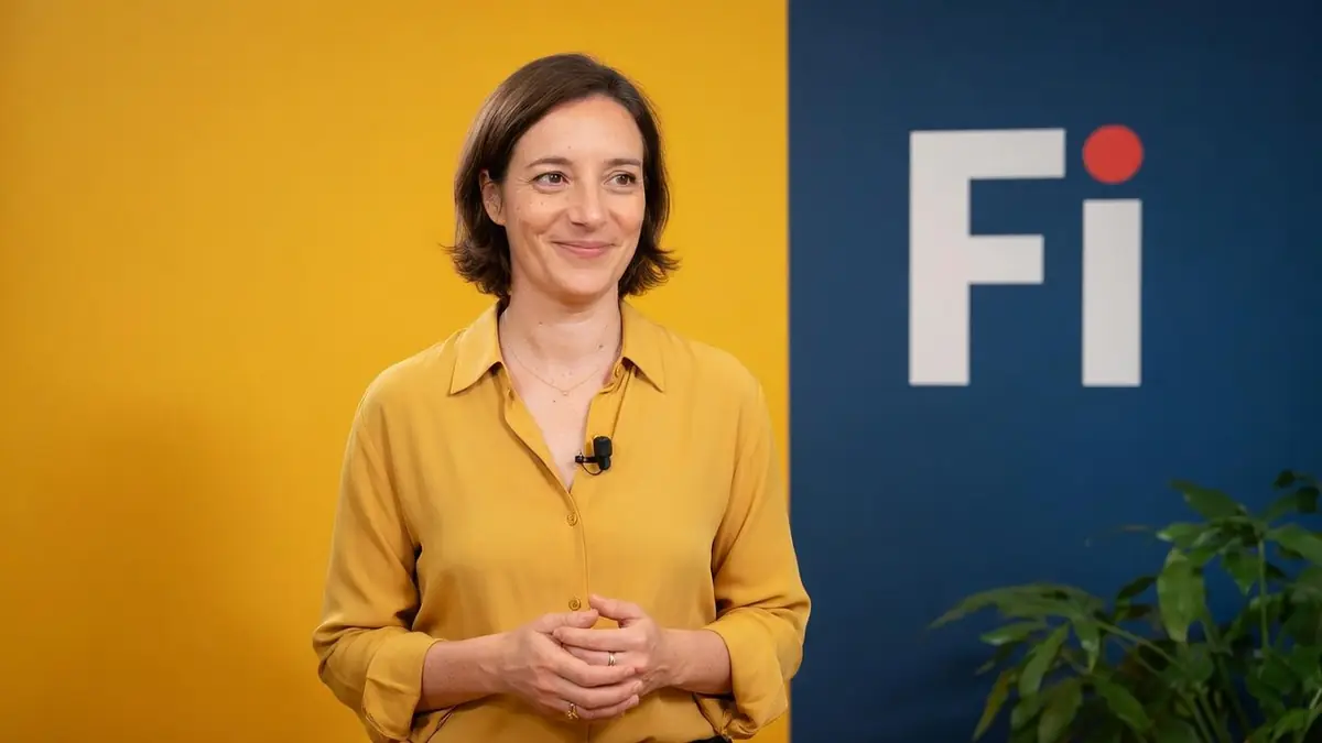 Céline Asselot se tient les mains jointes devant un fond jaune et bleu.