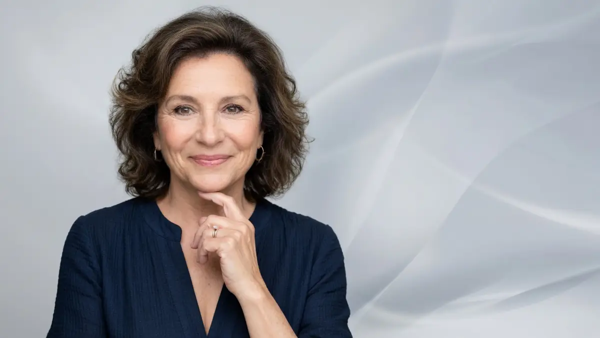 Portrait souriant et élégant de Laurence Jeanneret posant sur un fond gris neutre