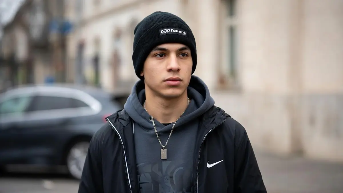 Un jeune homme porte un bonnet Kalenji noir dans la rue avec un sweat à capuche et une veste de sport