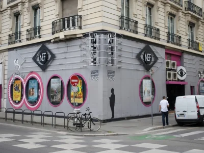 Façade d'angle grise avec des affiches de films sur le bâtiment du cinéma La Nef situé en ville