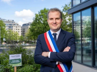Raphaël Adam se tient les bras croisés avec une écharpe tricolore devant un immeuble moderne