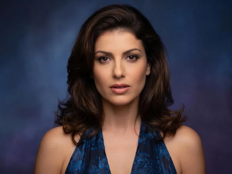 Karen Lancaume avec cheveux bruns et top bleu dans un portrait sur fond dégradé