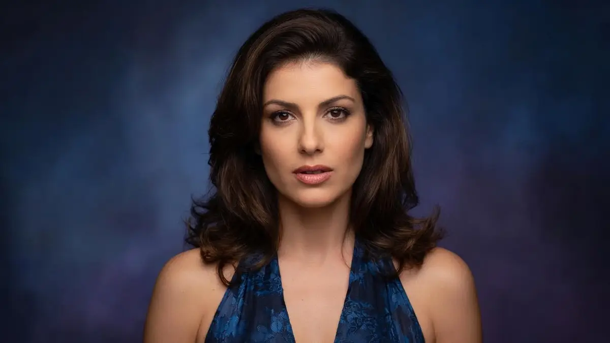 Karen Lancaume avec cheveux bruns et top bleu dans un portrait sur fond dégradé